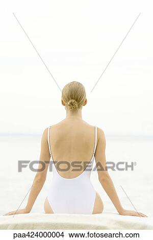 Picture - Female in bathing suit sitting on lounge chair, rear view. Fotosearch