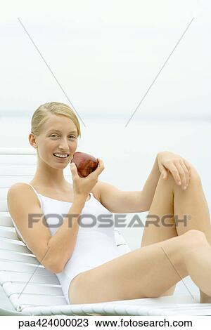 Teenage girl in swimsuit sitting on lounge chair, holding apple View Large Photo Image Stock Image - Teenage girl in swimsuit sitting on lounge chair, holding apple. Fotosearch