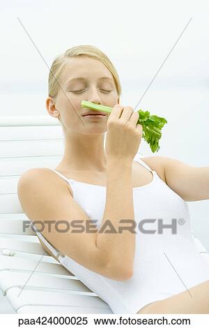 Teenage girl in swimsuit sitting on lounge chair, smelling stalk of celery View Large Photo Image Stock Photography - Teenage girl in swimsuit sitting on lounge chair, smelling stalk of celery. Fotosearch