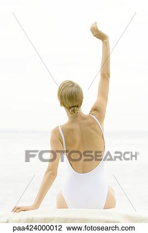 Stock Image - Teenage girl sitting with arm raised, wearing bathing suit, rear view. Fotosearch