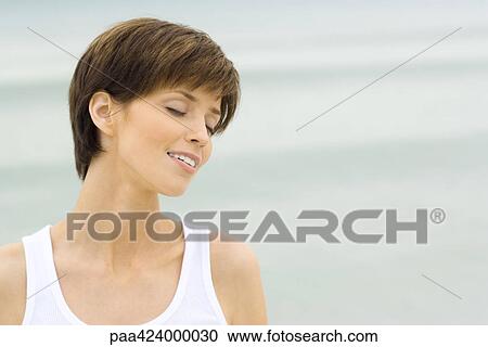 Young woman, eyes closed, sea in background View Large Photo Image Stock Image - Young woman, eyes closed, sea in background. Fotosearch