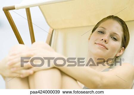 Young woman sitting in lounge chair, hugging knees and smiling View Large Photo Image Stock Photo - Young woman sitting in lounge chair, hugging knees and smiling. Fotosearch