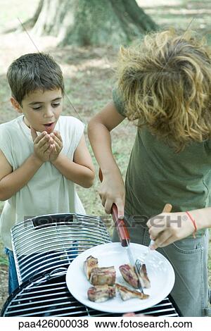 Boy cutting up piece of grilled meat while second boy watches View Large Photo Image Stock Photo - Boy cutting up piece of grilled meat while second boy watches. Fotosearch