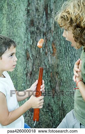 Boy holding hot dog on end of large fork, showing friend View Large Photo Image Stock Photo - Boy holding hot dog on end of large fork, showing friend . Fotosearch