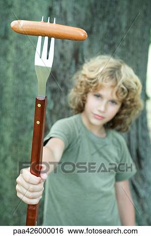 Boy holding hot dog on end of large fork View Large Photo Image Stock Photograph - Boy holding hot dog on end of large fork . Fotosearch