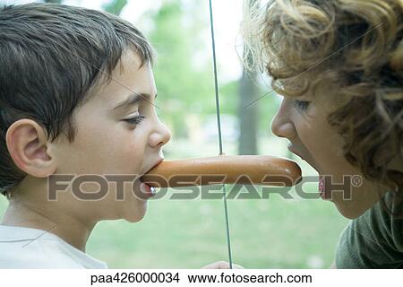 Boy holding hotdog in mouth while second boy takes bite out of other end View Large Photo Image Picture - Boy holding hotdog in mouth while second boy takes bite out of other end. Fotosearch