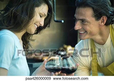 Stock Photo - Couple clinking glasses of wine in front of grilling food. Fotosearch