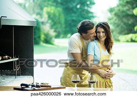 Couple having cookout, man hugging woman from behind View Large Photo Image Stock Photograph - Couple having cookout, man hugging woman from behind. Fotosearch