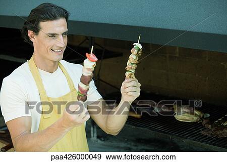 Man holding up two kebabs View Large Photo Image Stock Photo - Man holding up two kebabs. Fotosearch