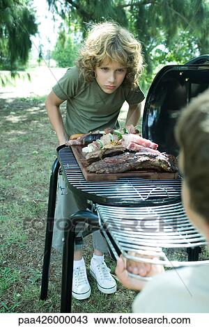 Two boys standing at either end of barbecue View Large Photo Image Stock Image - Two boys standing at either end of barbecue. Fotosearch