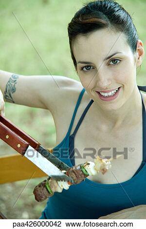 Woman holding up grilled kebab, smiling at camera View Large Photo Image Stock Image - Woman holding up grilled kebab, smiling at camera. Fotosearch