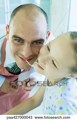 Father and daughter holding ends of noodle in mouths, smiling View Large Photo Image Stock Image - Father and daughter holding ends of noodle in mouths, smiling. Fotosearch