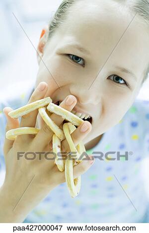 Girl eating circular cookies from fingers, looking at camera View Large Photo Image Stock Photo - Girl eating circular cookies from fingers, looking at camera. Fotosearch