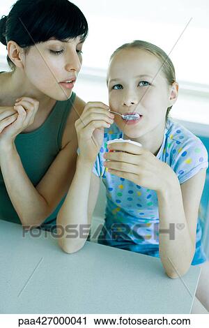 Girl eating yogurt while woman watches View Large Photo Image Stock Image - Girl eating yogurt while woman watches. Fotosearch
