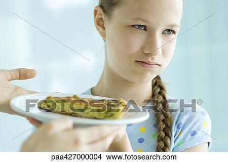 Hands holding up slice of quiche toward girl, girl making face and looking away View Large Photo Image Picture - Hands holding up slice of quiche toward girl, girl making face and looking away. Fotosearch