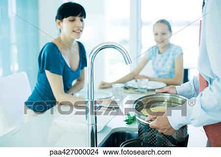 Man draining pasta while woman and girl watch View Large Photo Image Picture - Man draining pasta while woman and girl watch. Fotosearch