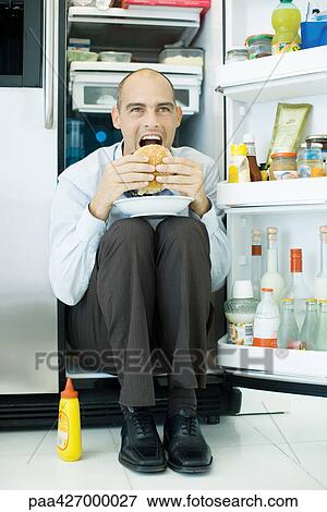 Man sitting inside refrigerator, eating sandwich View Large Photo Image Stock Photo - Man sitting inside refrigerator, eating sandwich. Fotosearch