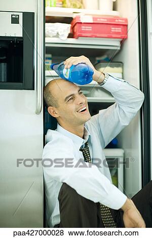 Man sitting next to open refrigerator door, holding bottle of water against forehead View Large Photo Image Stock Photo - Man sitting next to open refrigerator door, holding bottle of water against forehead. Fotosearch
