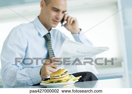 Man using phone and reading newspaper, hamburger on table in foreground View Large Photo Image Stock Image - Man using phone and reading newspaper, hamburger on table in foreground. Fotosearch