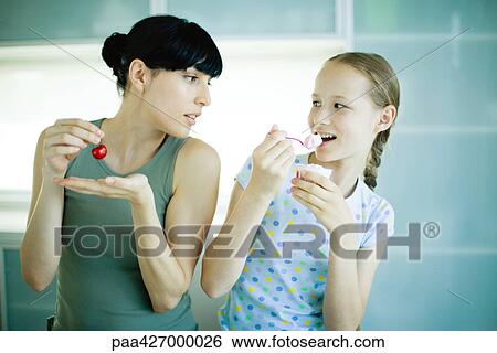 Woman eating cherry, watching girl eating yogurt View Large Photo Image Stock Photograph - Woman eating cherry, watching girl eating yogurt. Fotosearch