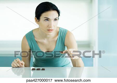 Stock Photo - Woman eating chunks of chocolate, looking away. Fotosearch