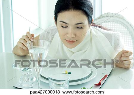 Woman sitting at set table, wearing napkin around neck, vitamins on plate View Large Photo Image Stock Photo - Woman sitting at set table, wearing napkin around neck, vitamins on plate. Fotosearch