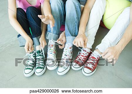 Friends sitting on floor, wearing canvas shoes, tying laces, low section View Large Photo Image Stock Photograph - Friends sitting on floor, wearing canvas shoes, tying laces, low section. Fotosearch