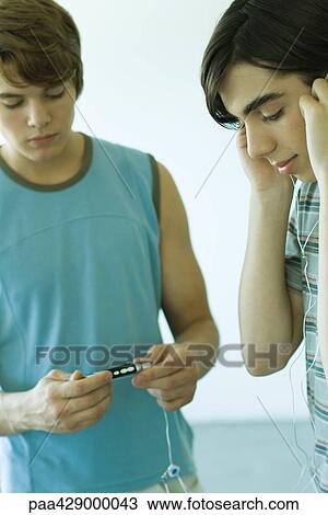 Stock Image - Teenage boys listening to MP3 player. Fotosearch