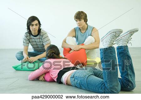 Stock Image - Teenage friends lying on cushions, chatting. Fotosearch