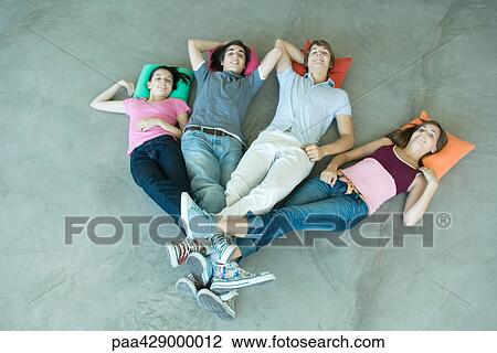 Stock Image - Teenage friends lying on floor with legs joined at ankles. Fotosearch