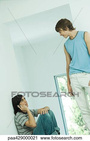 Stock Image - Teenage friends, one using cell phone while the other watches . Fotosearch