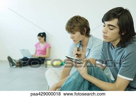Stock Photo - Teenage friends sitting on floor, one writing in notebook. Fotosearch