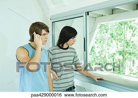 Stock Photograph - Teenage friends standing by window, one using laptop. Fotosearch