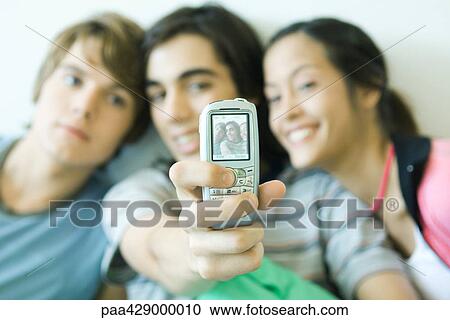 Teenage friends taking photo with cell phone, focus on phone in foreground View Large Photo Image Stock Image - Teenage friends taking photo with cell phone, focus on phone in foreground. Fotosearch