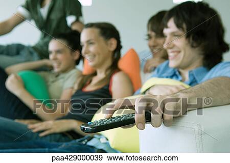 Teenage friends watching TV together, focus on remote control in foreground View Large Photo Image Stock Photo - Teenage friends watching TV together, focus on remote control in foreground. Fotosearch