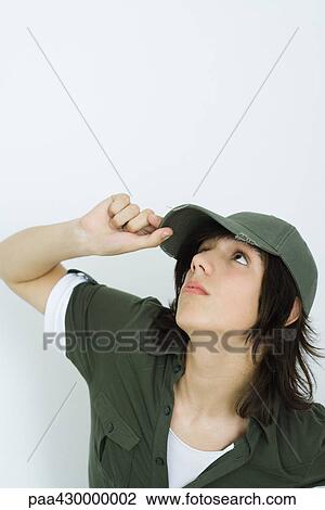 Stock Image - Teenage boy adjusting cap, looking up. Fotosearch