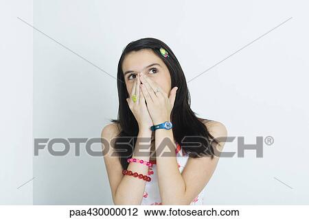 Stock Image - Teenage girl, hands over nose and mouth, looking up, portrait. Fotosearch