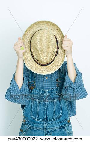 Stock Image - Teenage girl holding hat in front of face, portrait. Fotosearch
