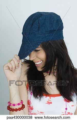Stock Photo - Teenage girl pulling cap down, smiling, portrait. Fotosearch