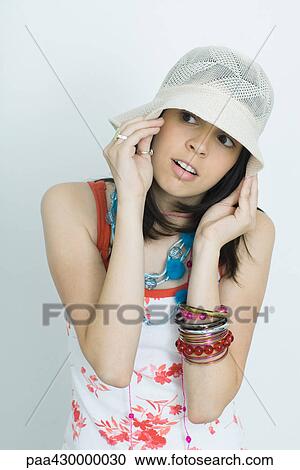 Stock Image - Teenage girl pulling down hat, looking to the side, portrait. Fotosearch