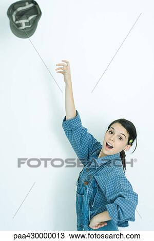 Stock Image - Teenage girl throwing hat into air, portrait. Fotosearch