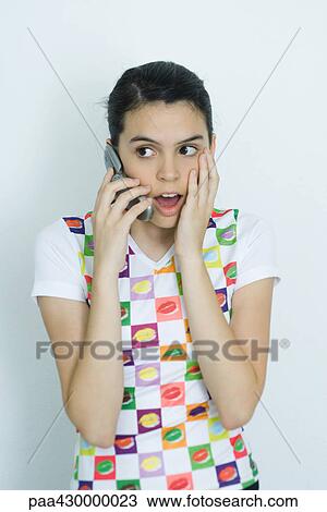Stock Image - Teenage girl using cell phone, making surprised face, portrait. Fotosearch
