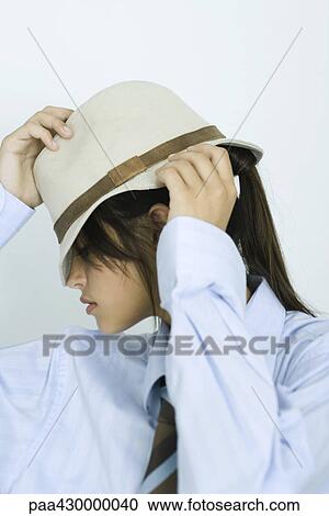 Stock Image - Teenage girl wearing shirt and tie, pulling hat down over eyes, portrait. Fotosearch