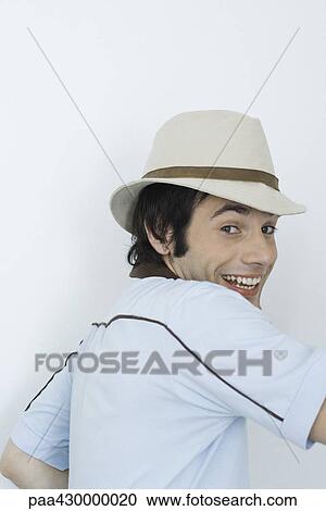 Young man wearing hat, smiling over shoulder at camera View Large Photo Image Stock Image - Young man wearing hat, smiling over shoulder at camera. Fotosearch