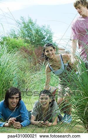 Group of young friends laughing outdoors, two lying on grass View Large Photo Image Stock Image - Group of young friends laughing outdoors, two lying on grass. Fotosearch