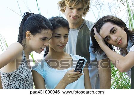 Group of young friends looking at cell phone together View Large Photo Image Stock Photograph - Group of young friends looking at cell phone together. Fotosearch