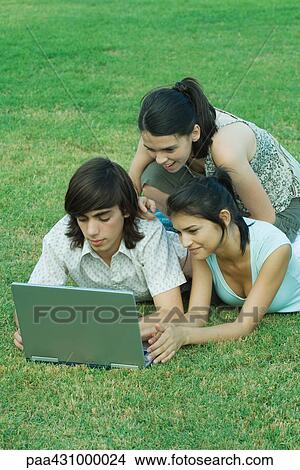 Picture - Group of young friends lying in grass using laptop. Fotosearch