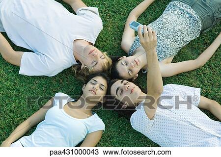 Group of young friends lying on grass with heads together, eyes closed, one taking photo with cell phone View Large Photo Image Stock Image - Group of young friends lying on grass with heads together, eyes closed, one taking photo with cell phone. Fotosearch