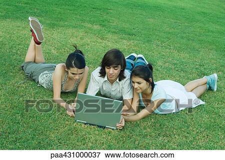 Group of young friends lying on grass, using laptop View Large Photo Image Stock Photo - Group of young friends lying on grass, using laptop. Fotosearch