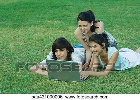 Group of young friends lying on grass together, using laptop View Large Photo Image Stock Photograph - Group of young friends lying on grass together, using laptop. Fotosearch